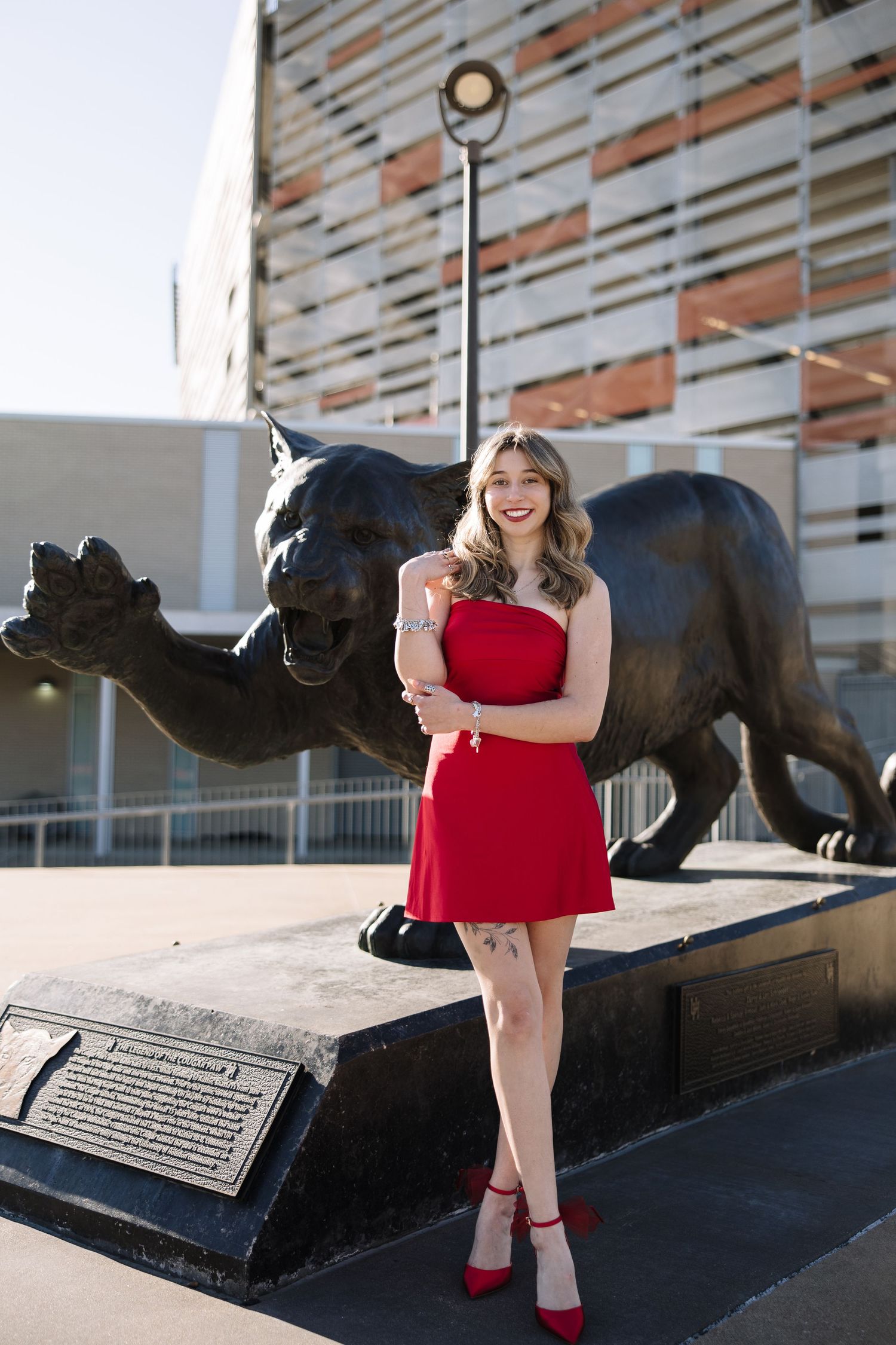 Woman in red strapless dress and heels posing by a black panther statue outside a stadium.