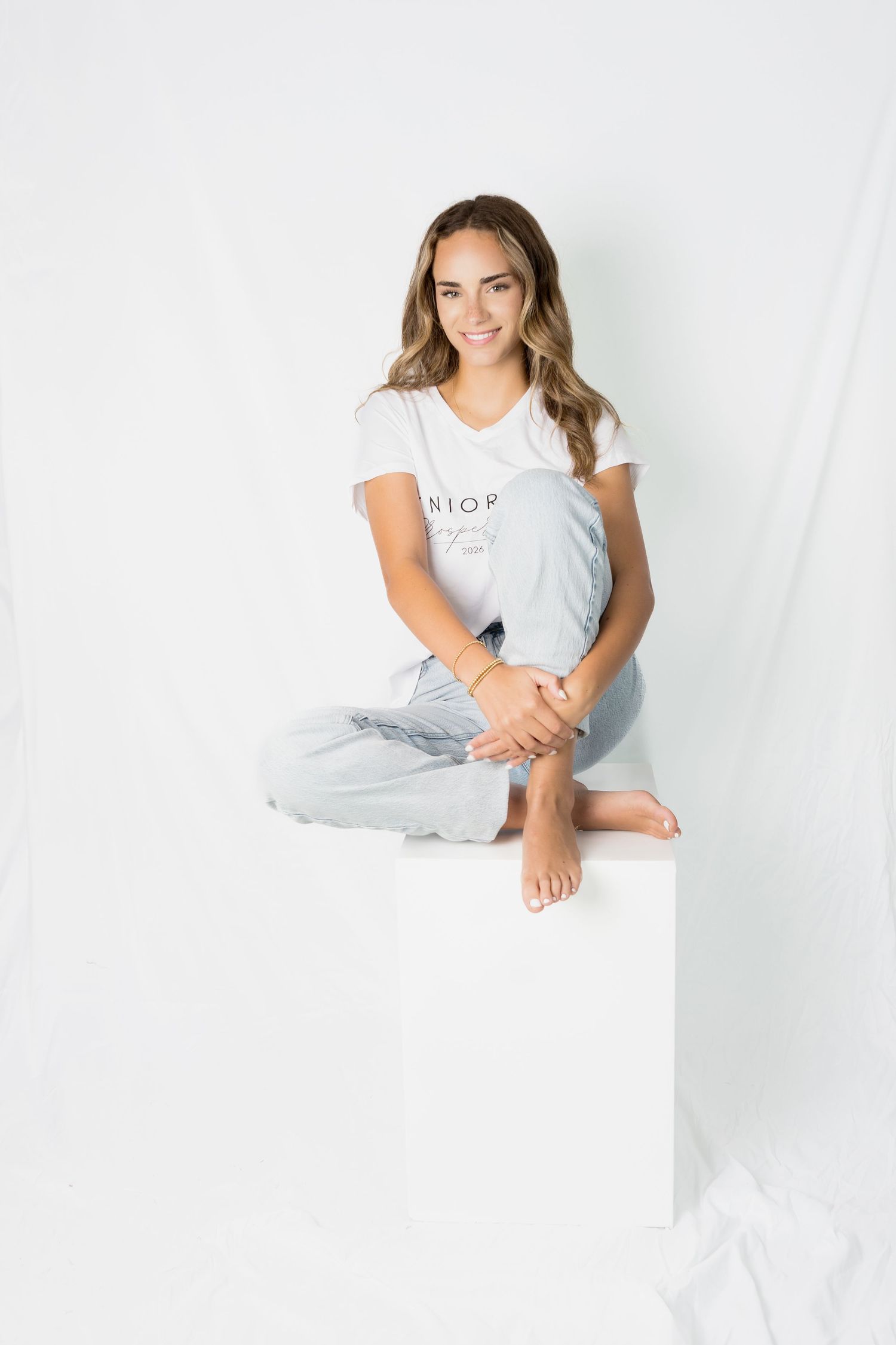 Person in casual attire poses against white backdrop in minimalist studio setting.
