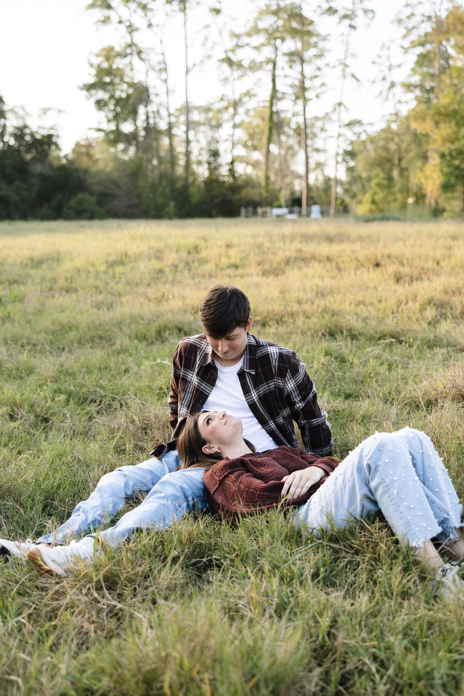 A couple relaxes together on a grassy hillside during golden hour in a natural outdoor setting.