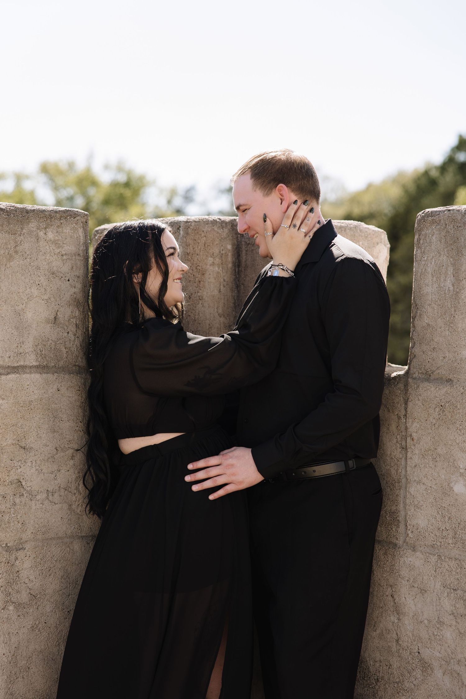 Couple in matching black outfits sharing a romantic moment against stone pillars outdoors.