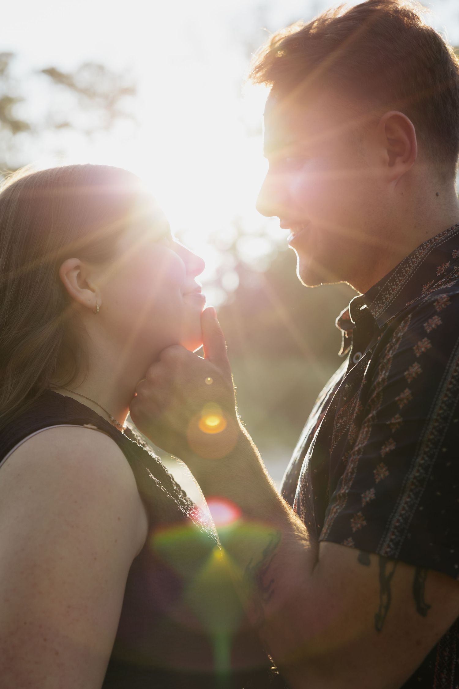 Silhouetted couple embracing in romantic sunset light with lens flare creating a dreamy atmosphere.