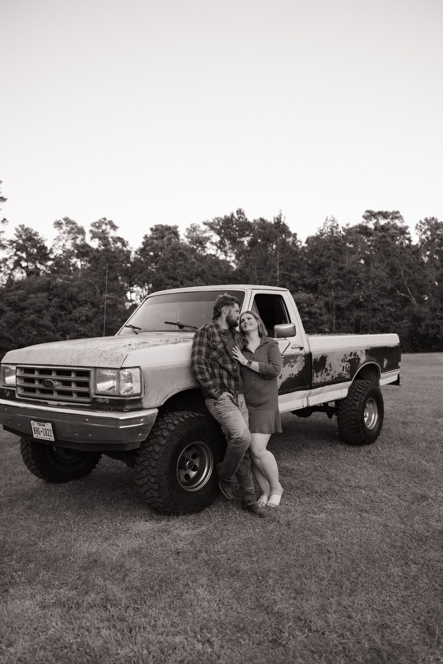 Black and white photos show someone crouched beside a vintage pickup truck parked on grassy field.
