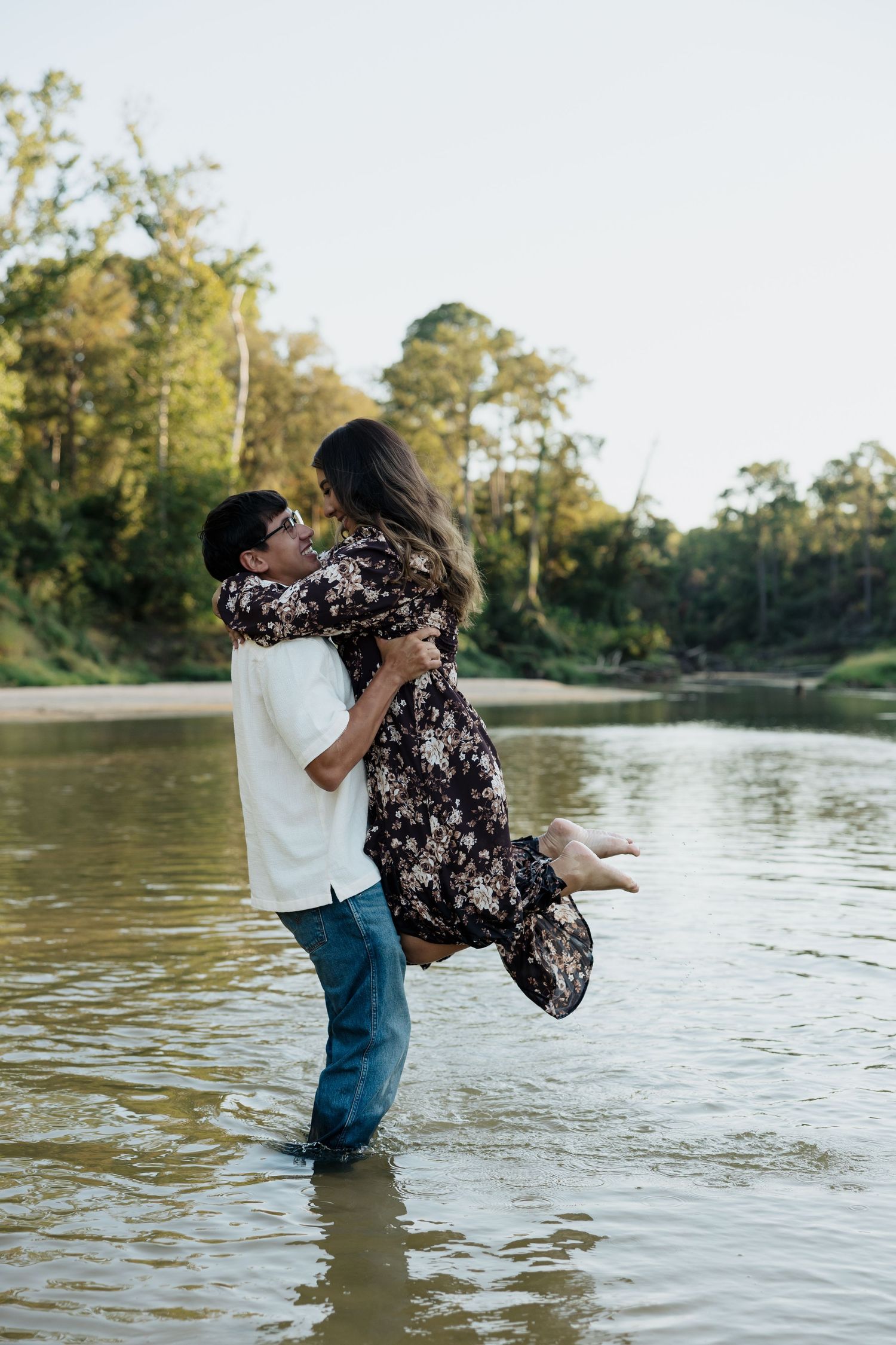A romantic couple embraces while standing in shallow lake water during a sunny outdoor photoshoot.