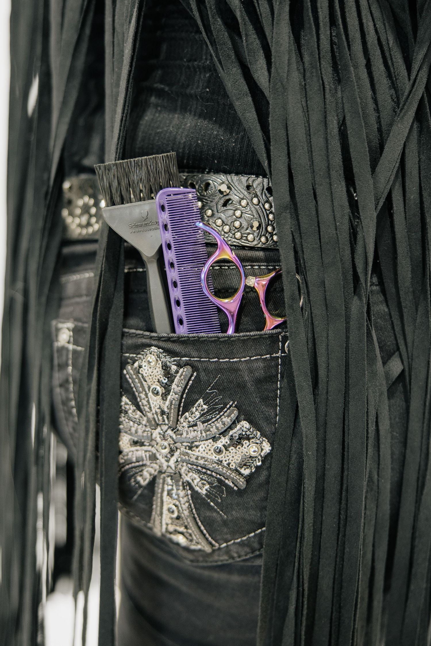 Decorative back pocket of dark jeans with purple comb and sparkly embellishments.