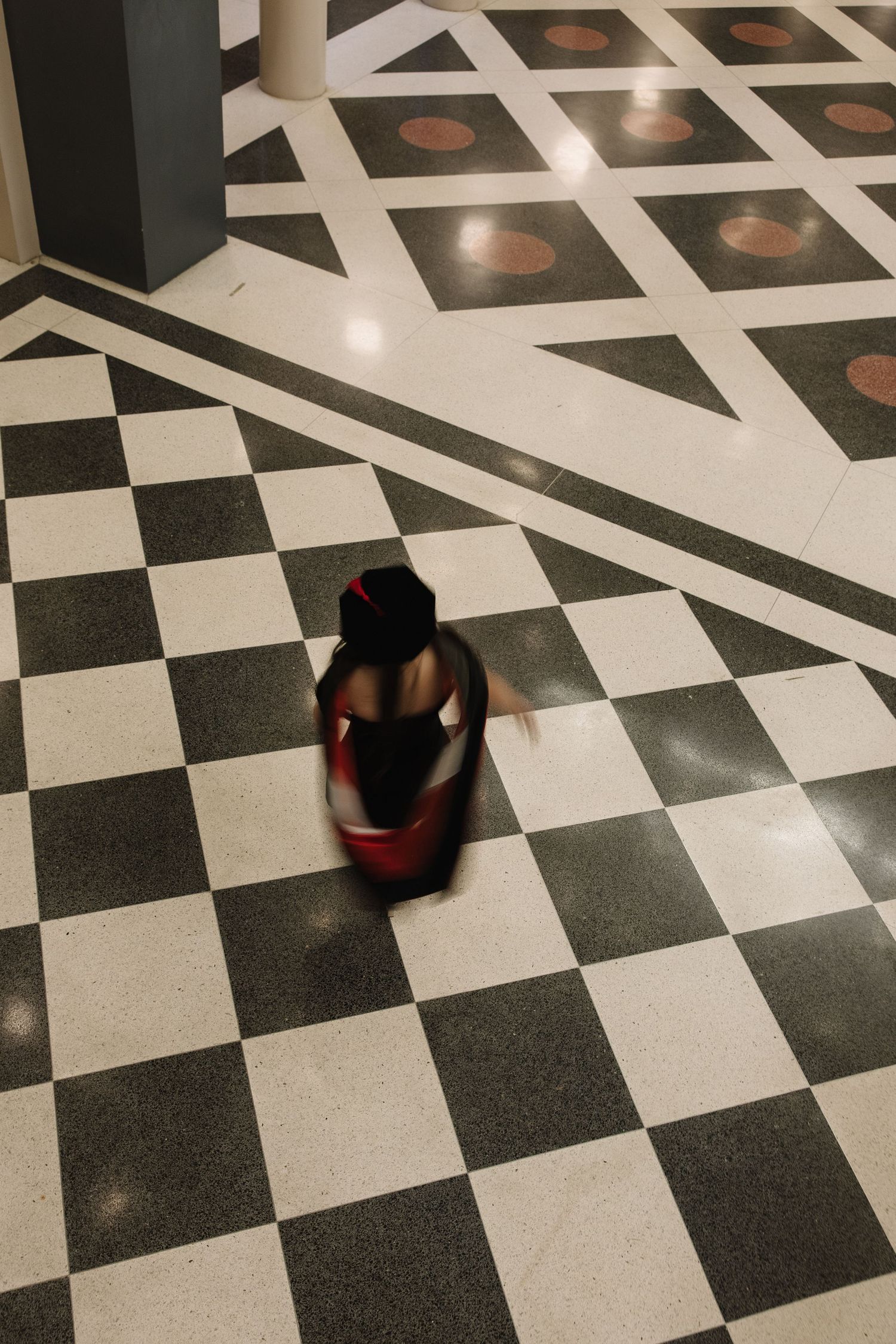 Blurred figure in red and black walking across a classic black and white checkered marble floor.