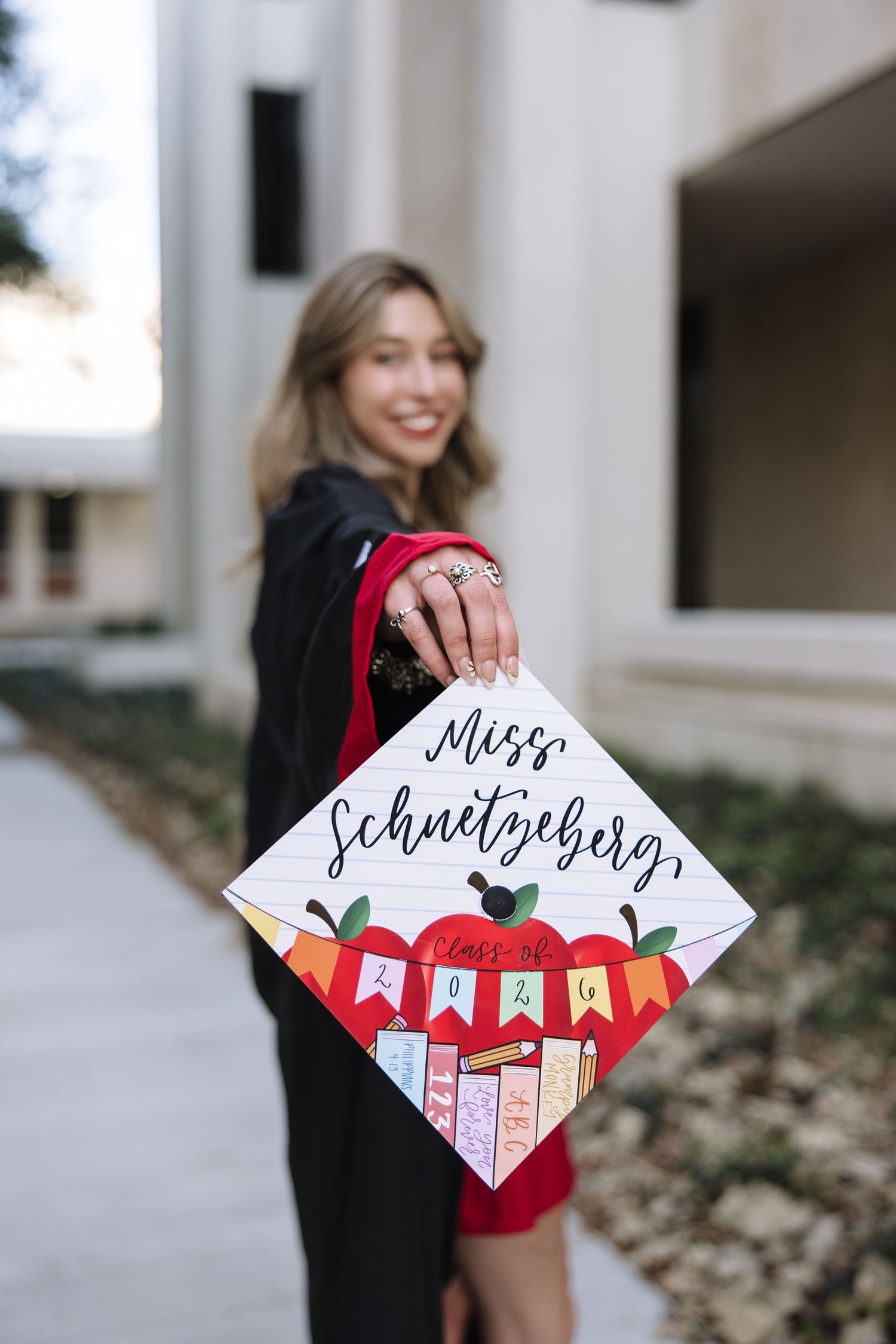 Graduate holds decorated cap reading Miss Schnetzberg Class of 2024 with apple and school themed design.