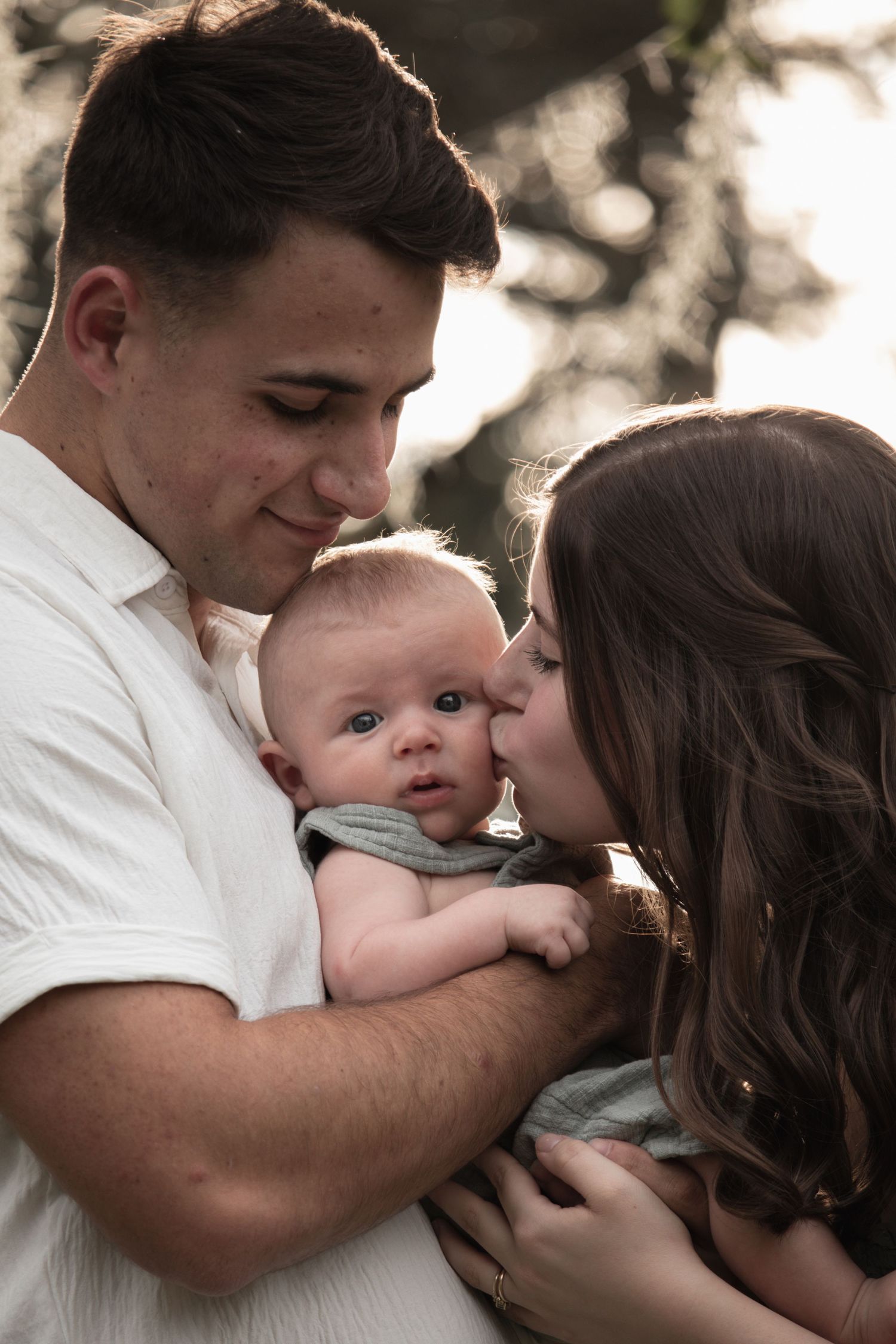 A tender family moment with parents cradling their baby outdoors at sunset.
