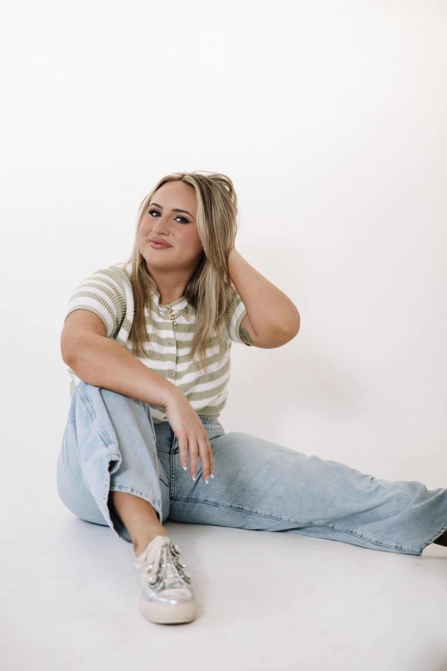 Model in casual striped top and light wash jeans poses casually on white backdrop.
