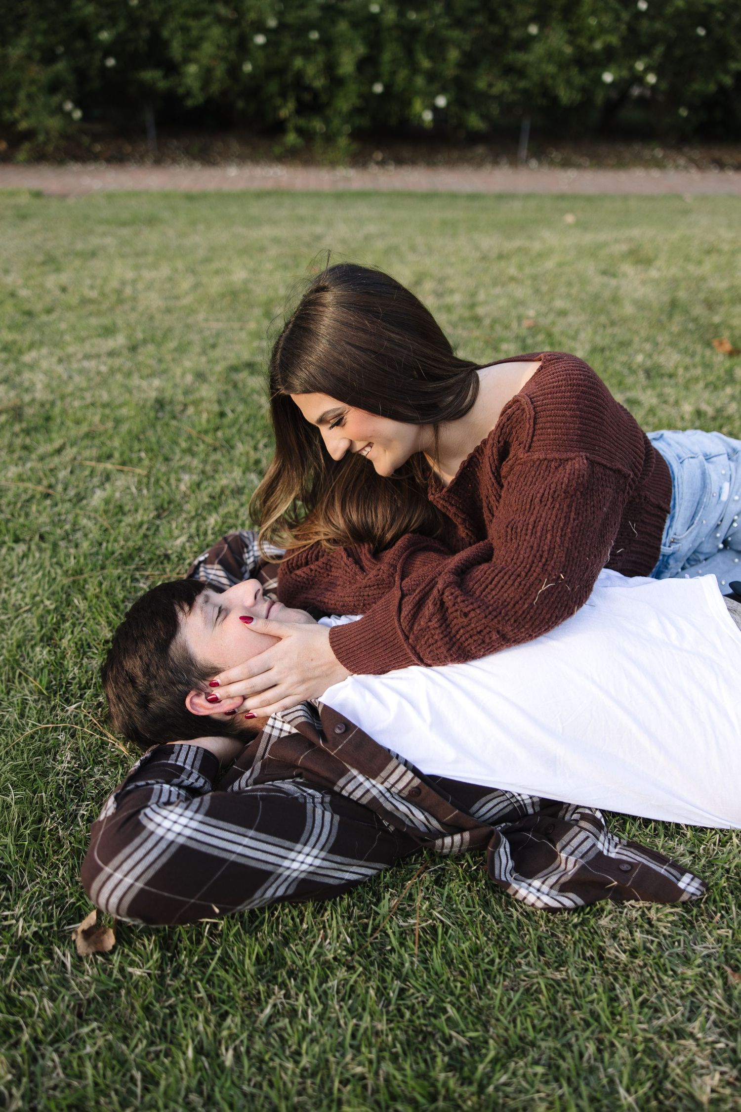 A couple lying together on green grass in a romantic outdoor photoshoot series.