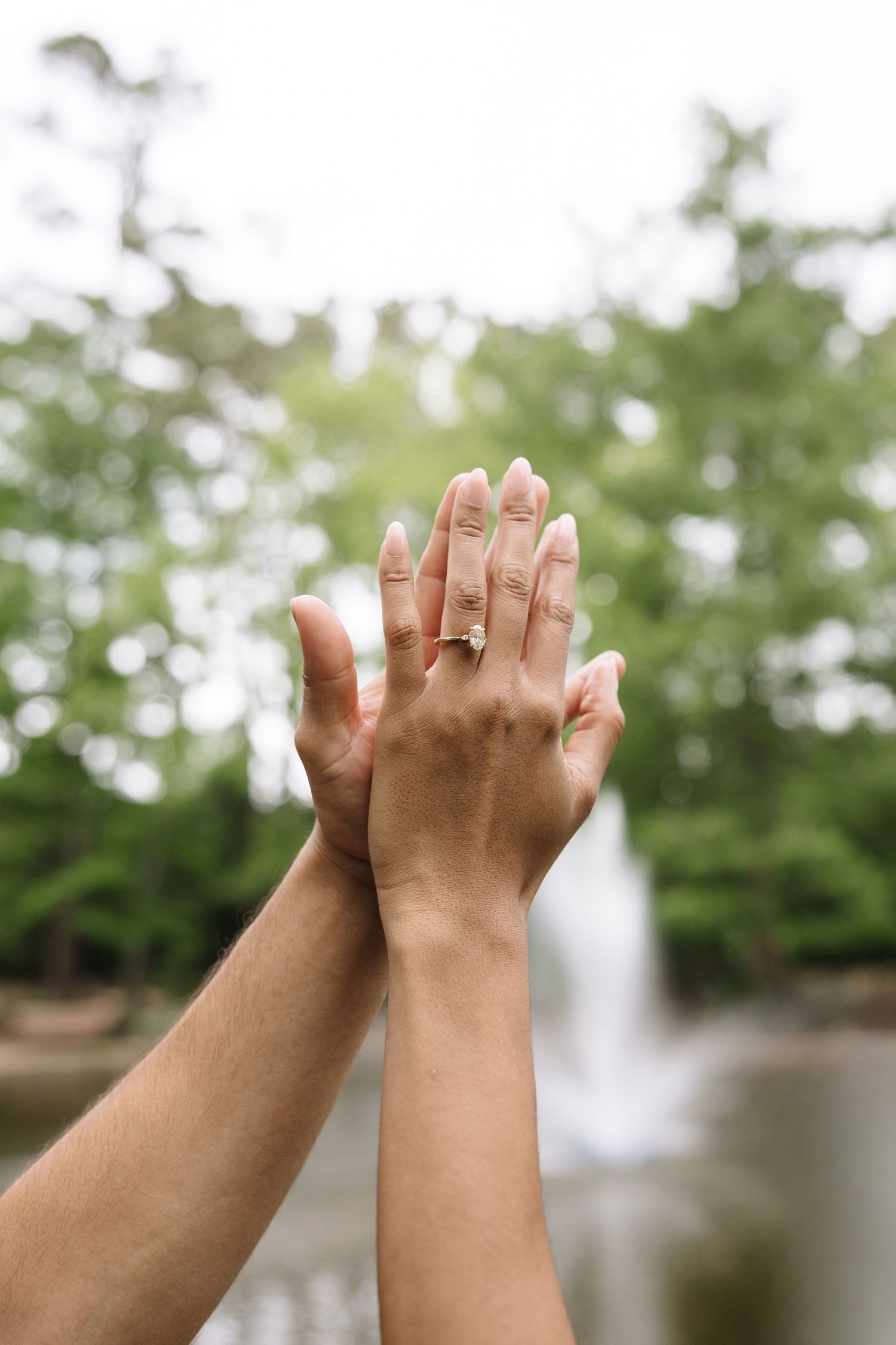 Close-up of hands raised showing an engagement ring with a waterfall backdrop.