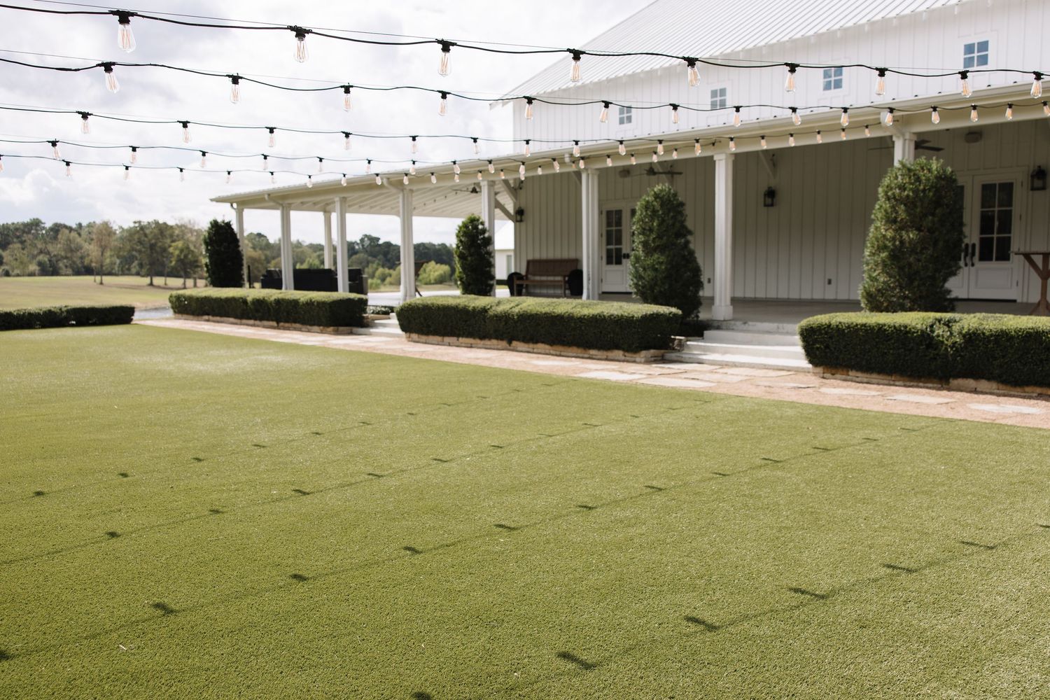 String lights hang above an elegant outdoor venue with manicured lawns and white columns creating a romantic atmosphere.