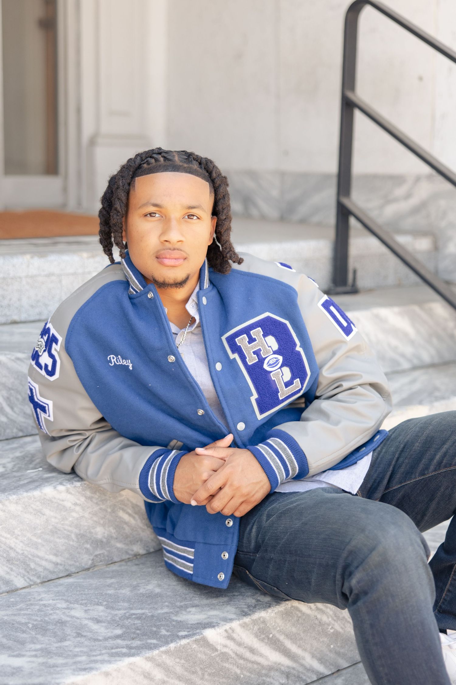 Casual portrait of person in blue letterman jacket lounging on steps.