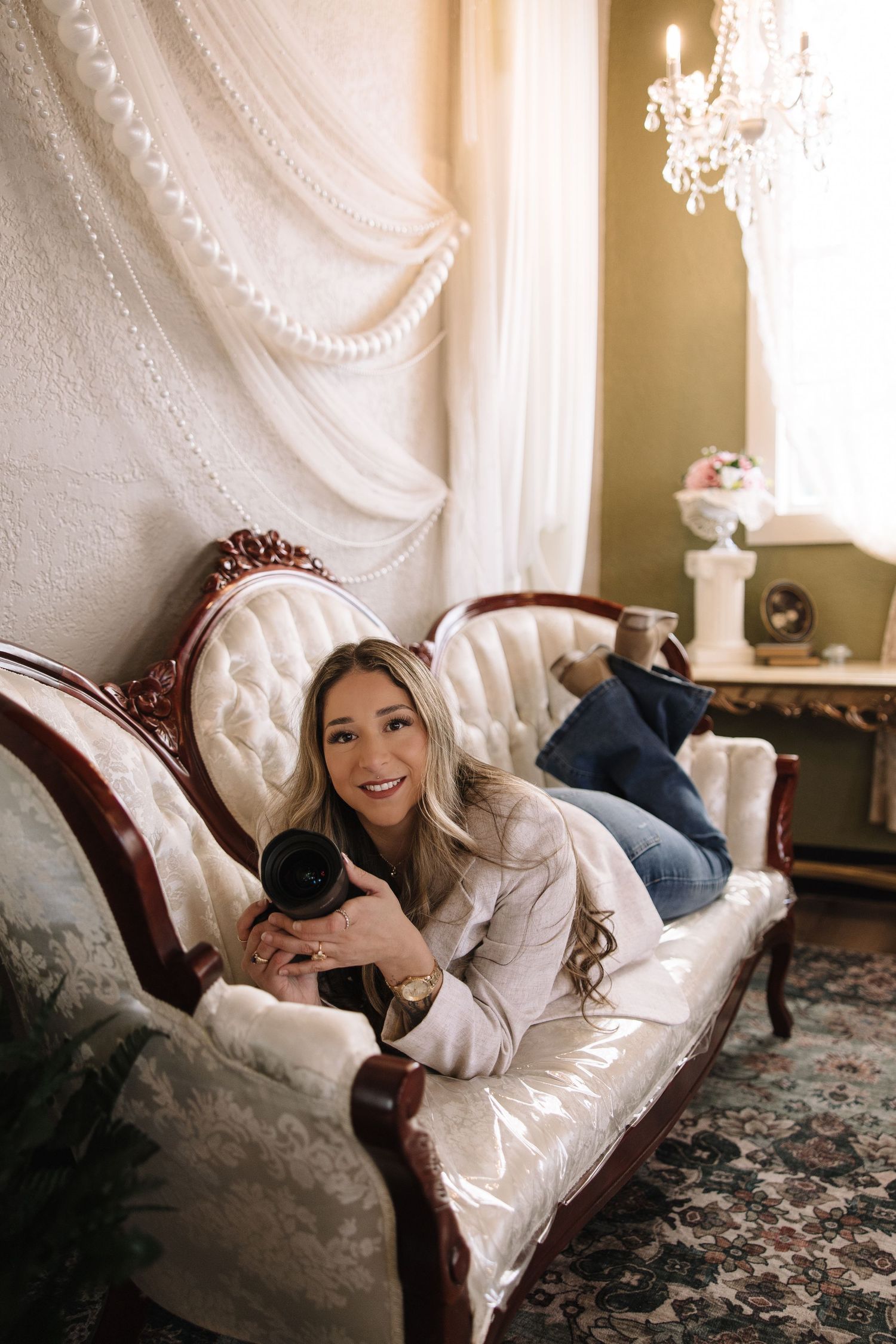 A photographer relaxes on a floral couch while taking photos in an elegant room with ornate white wall details.