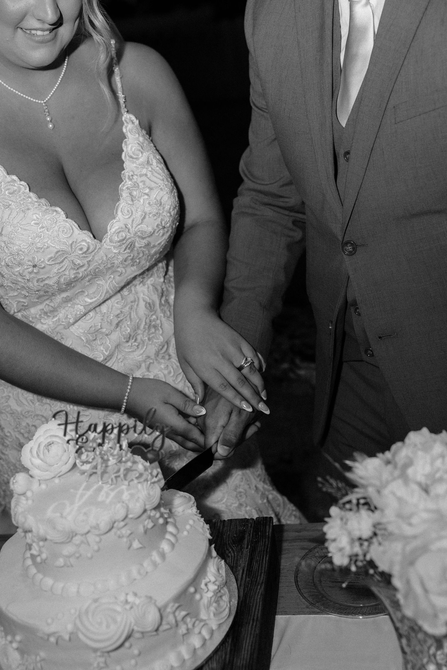 Bride and groom cutting white tiered wedding cake together in black and white photo.