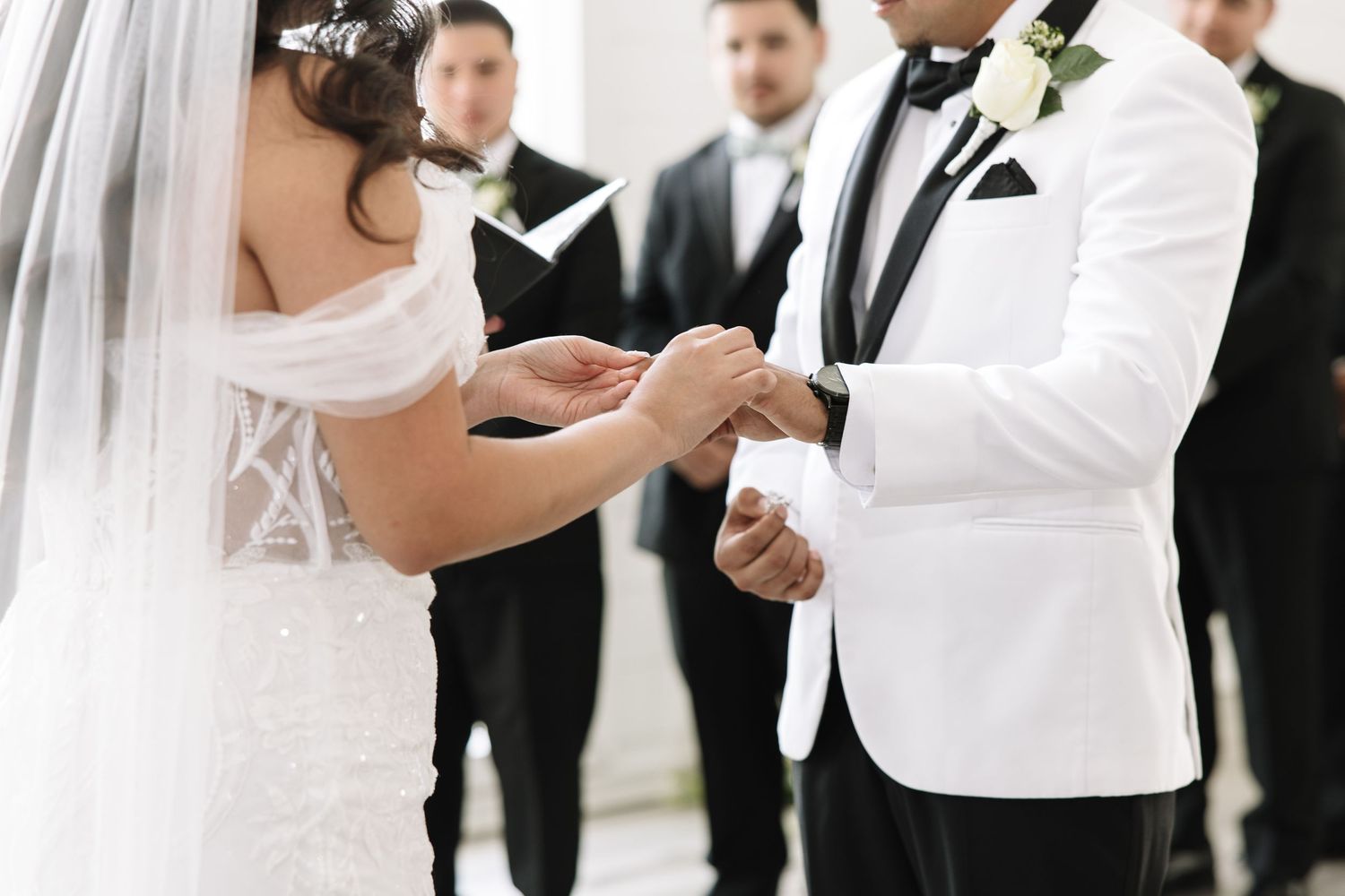 A couple exchanges rings during their wedding ceremony while surrounded by their wedding party.