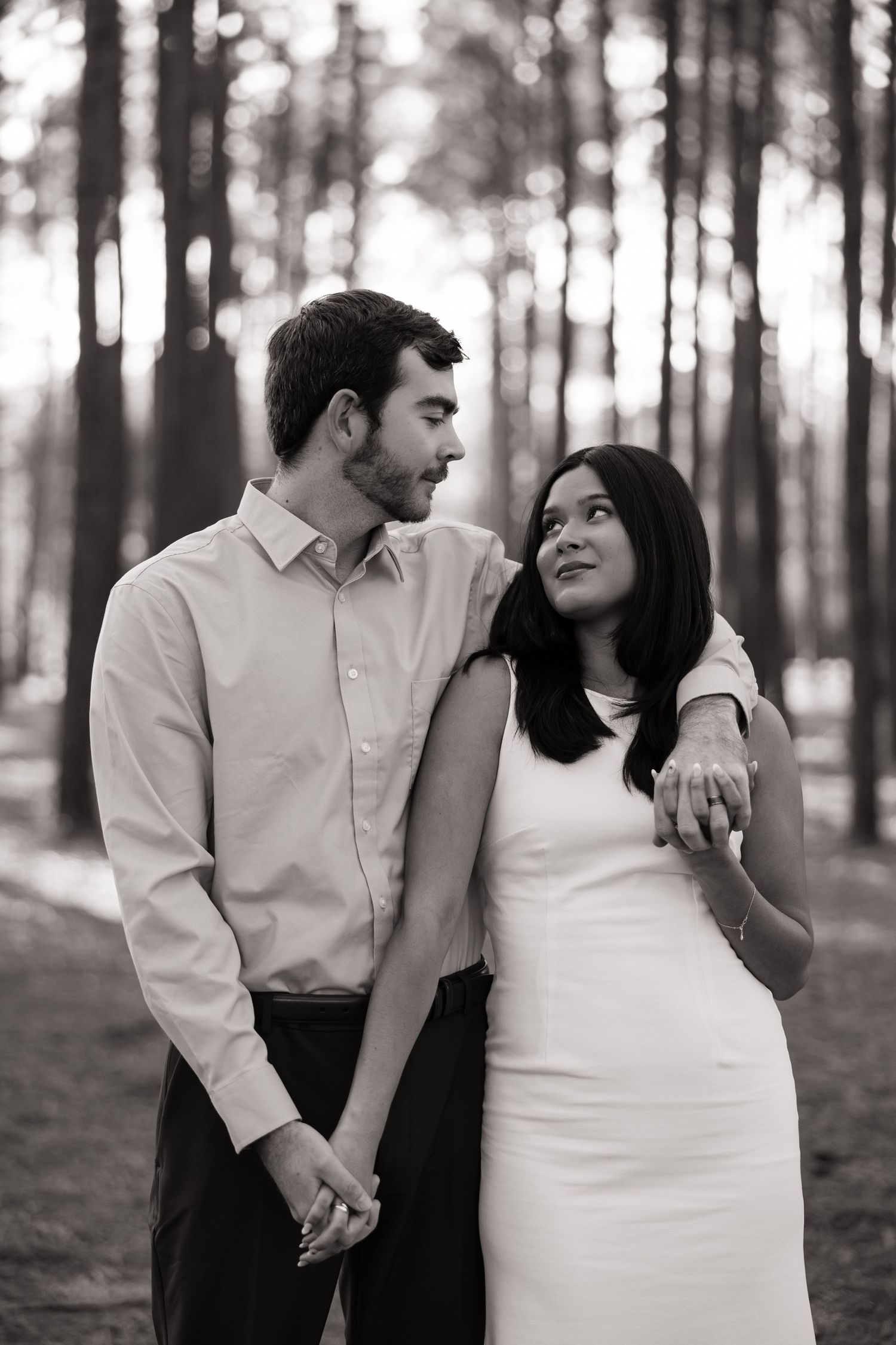 Black and white romantic engagement photos of a couple in a forest setting.