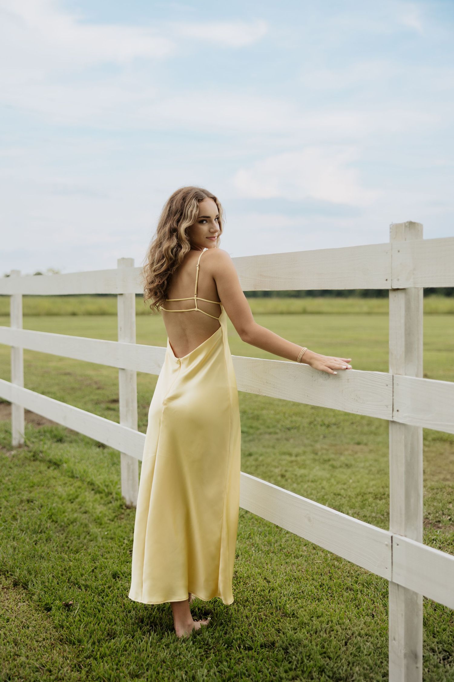 Yellow sundress flowing in the breeze beside a white fence in a pastoral setting.