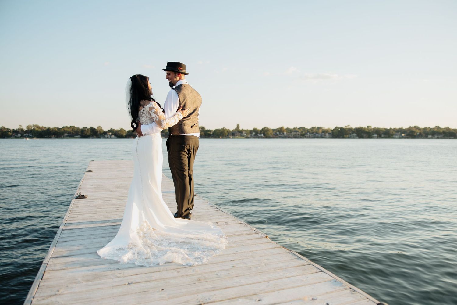 A couple shares a romantic moment on a wooden dock overlooking a serene lake at sunset.