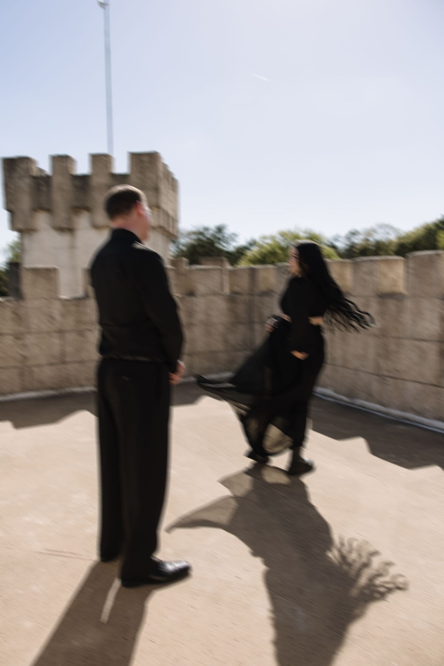 Two people in black attire on castle rooftop in motion blur photography.