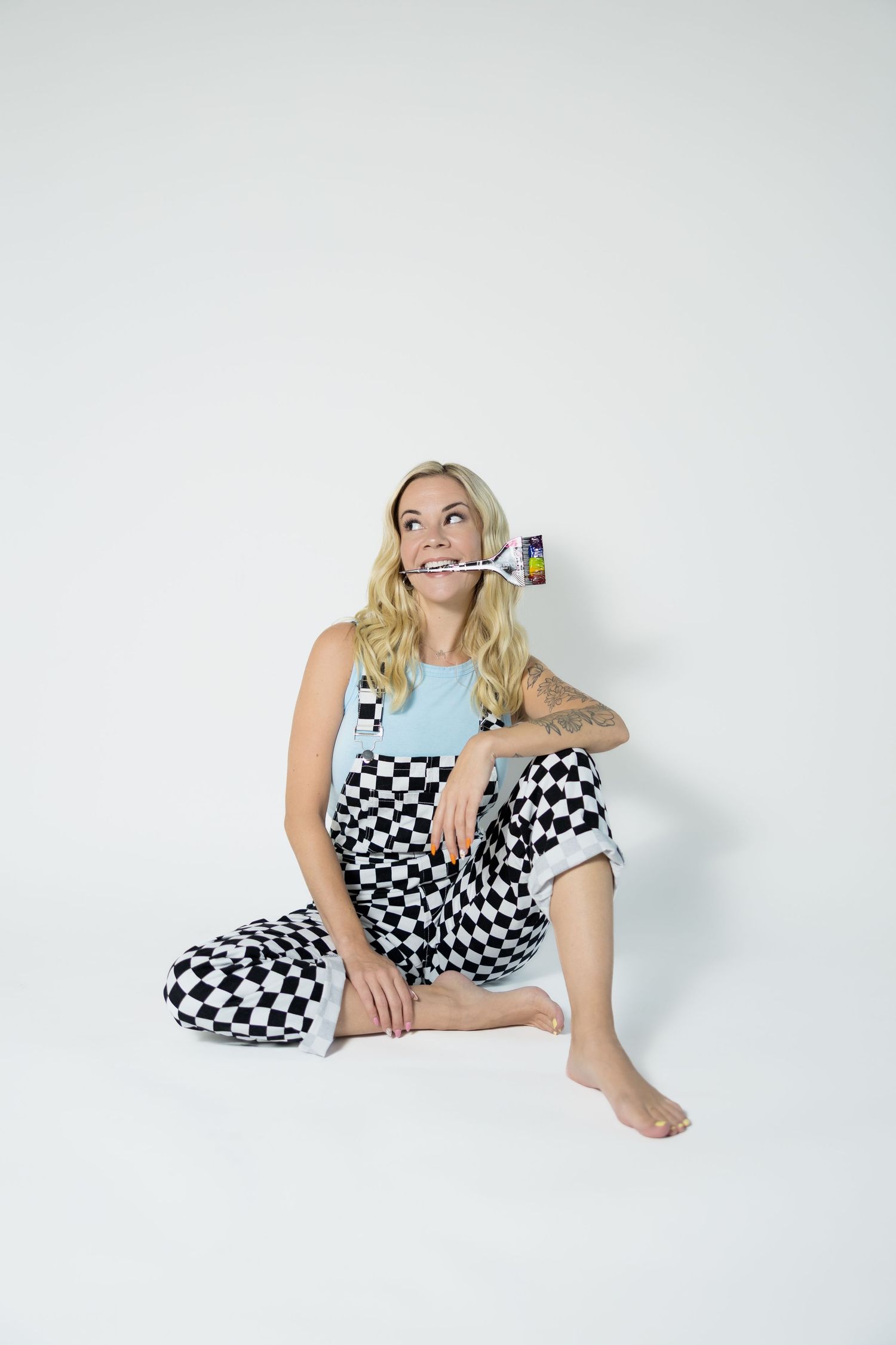 Person in checkered overalls and blue top sitting casually against white background with toothbrush.