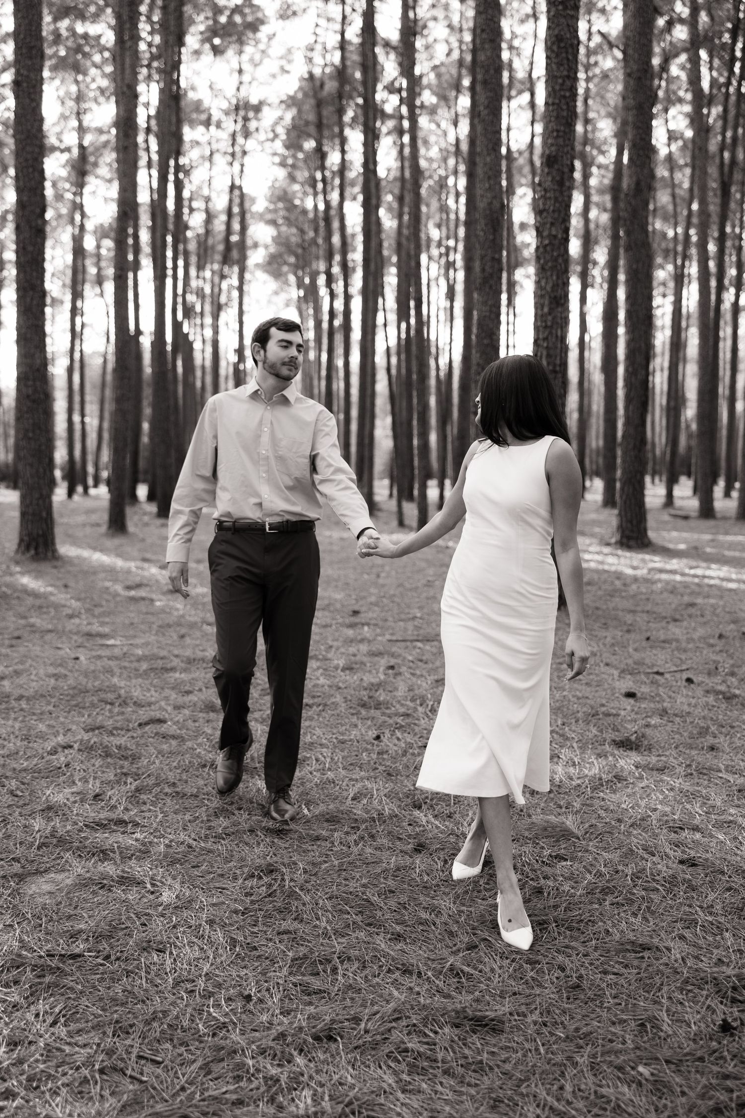 A couple walking hand in hand through a misty pine forest in black and white photography.