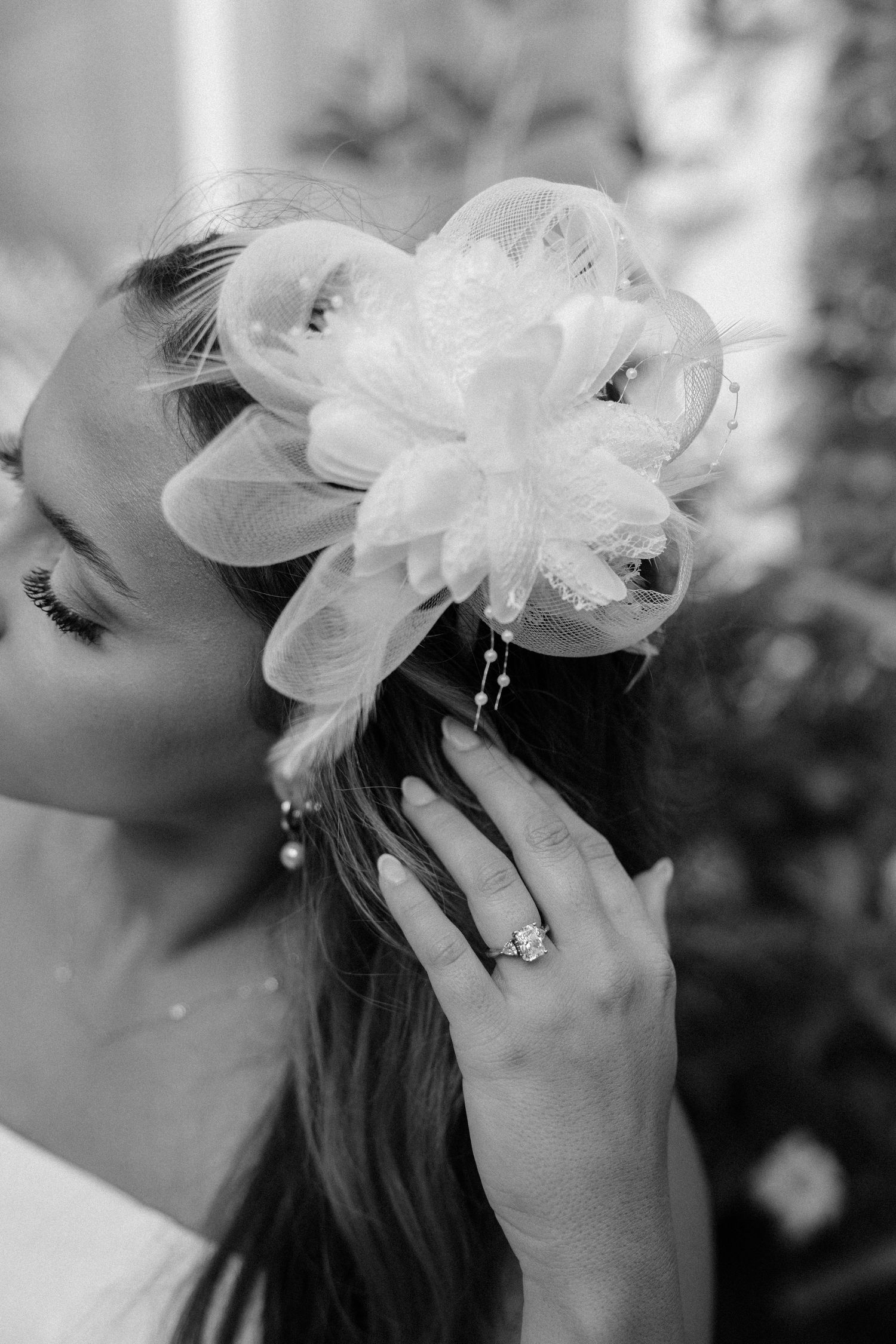 Black and white photo of a bride adjusting a floral hair accessory, showcasing her diamond engagement ring.
