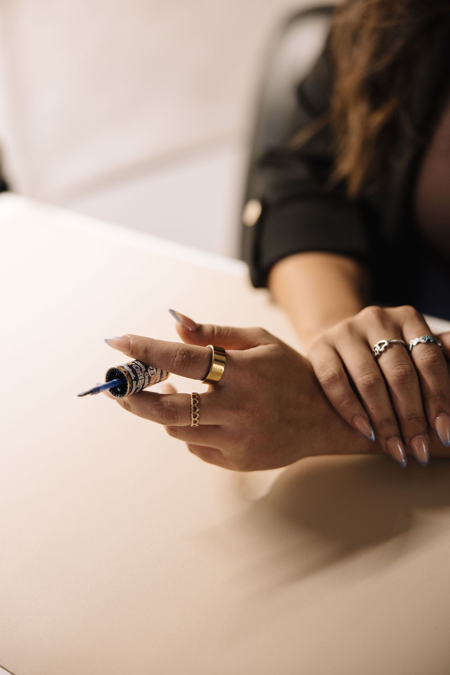 Close-up shots of hands wearing rings holding a pen against a white surface in a minimalist style.