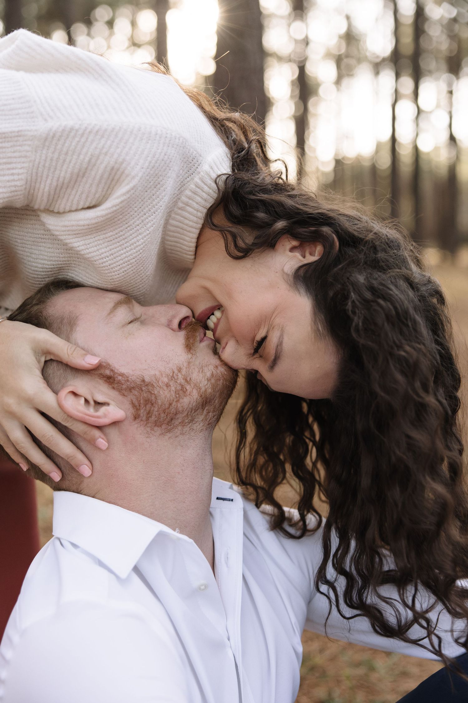 A romantic couple shares an intimate moment in a forest setting with soft natural lighting.