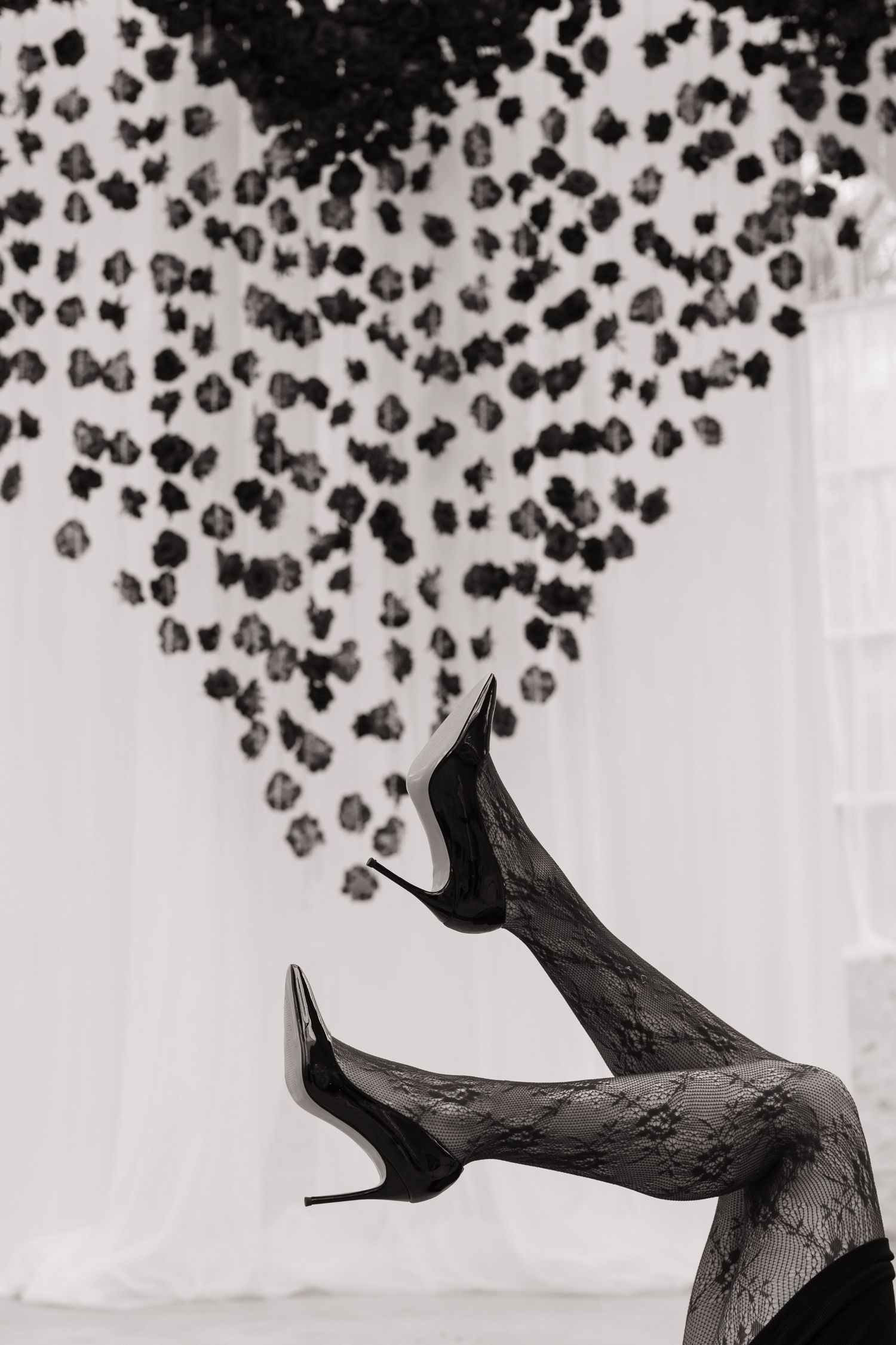A black high heel shoe photographed against a white background with scattered black dots above it.