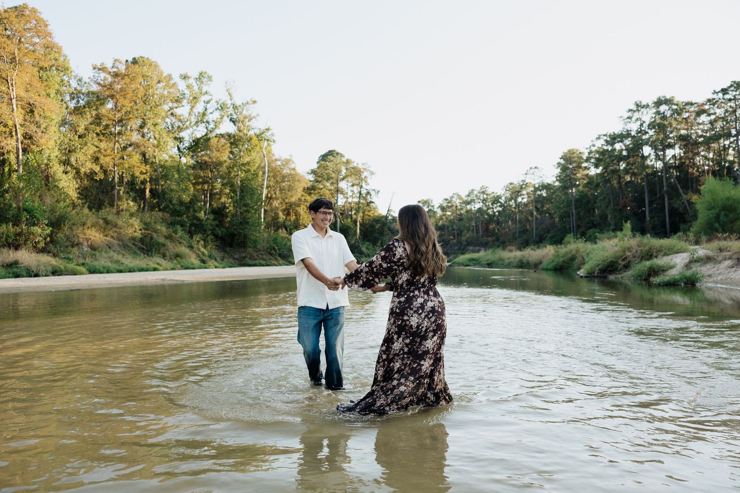 A couple stands in shallow river water during a romantic outdoor photoshoot at sunset.