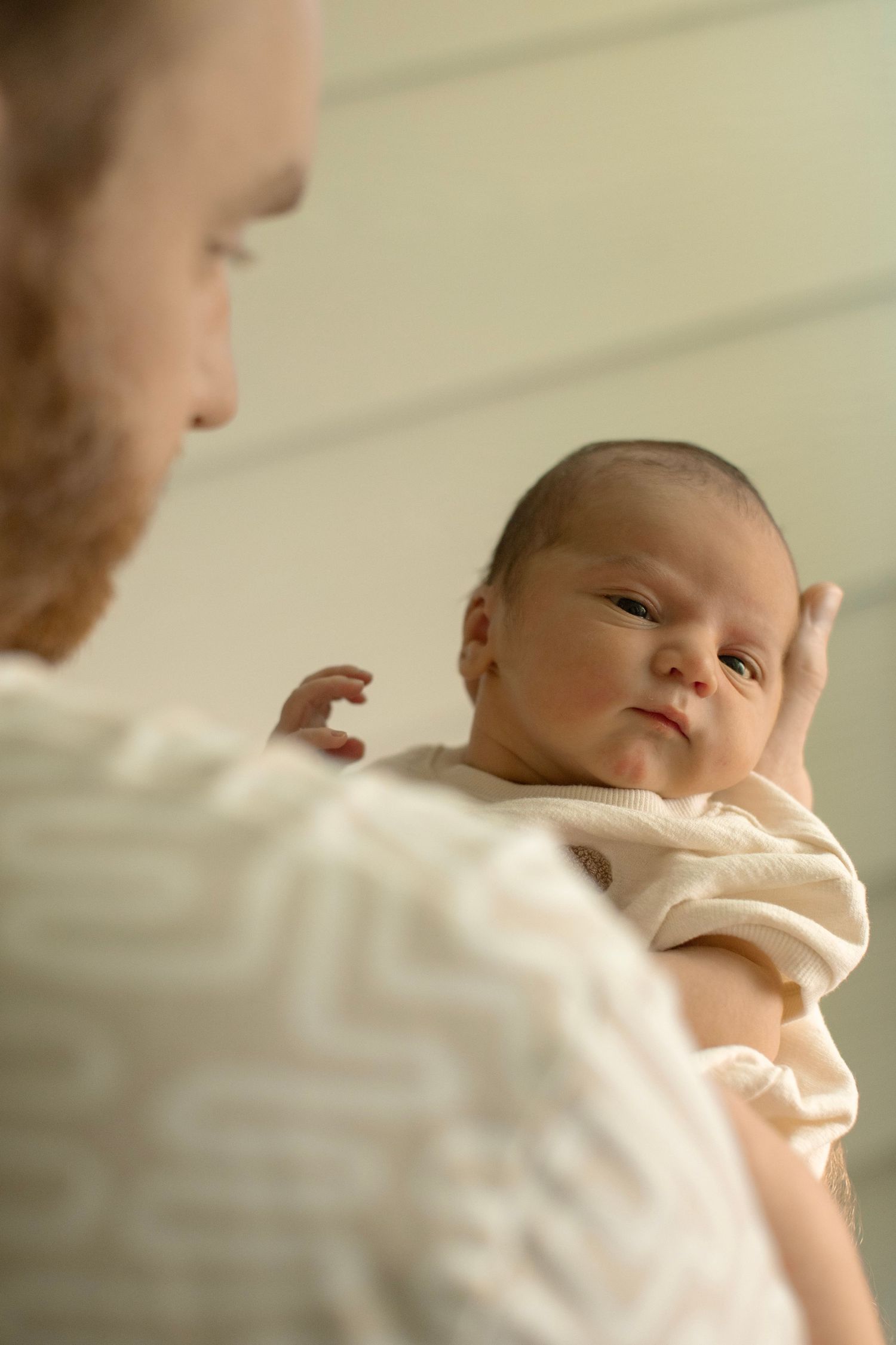 A tender moment between parent and newborn baby lying in soft cream-colored clothing.