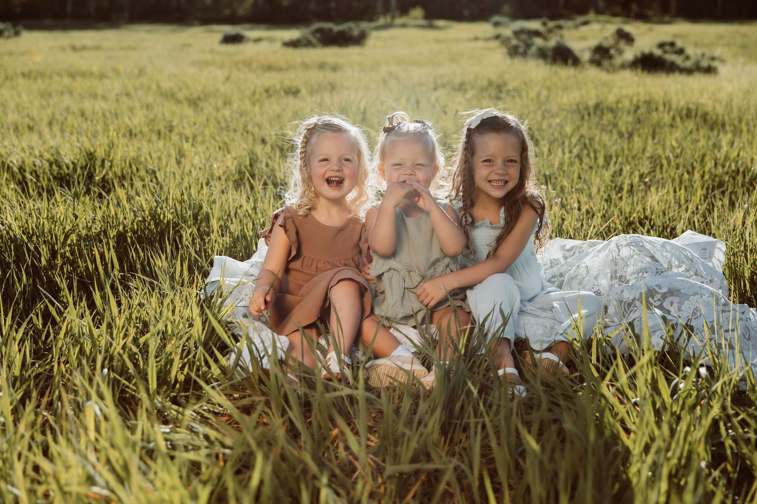 Siblings sitting together in a tall grass field during golden hour as light filters through the grass.