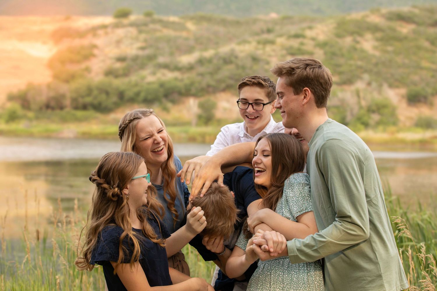 A joyful group laughing together outdoors by a lake during golden hour.