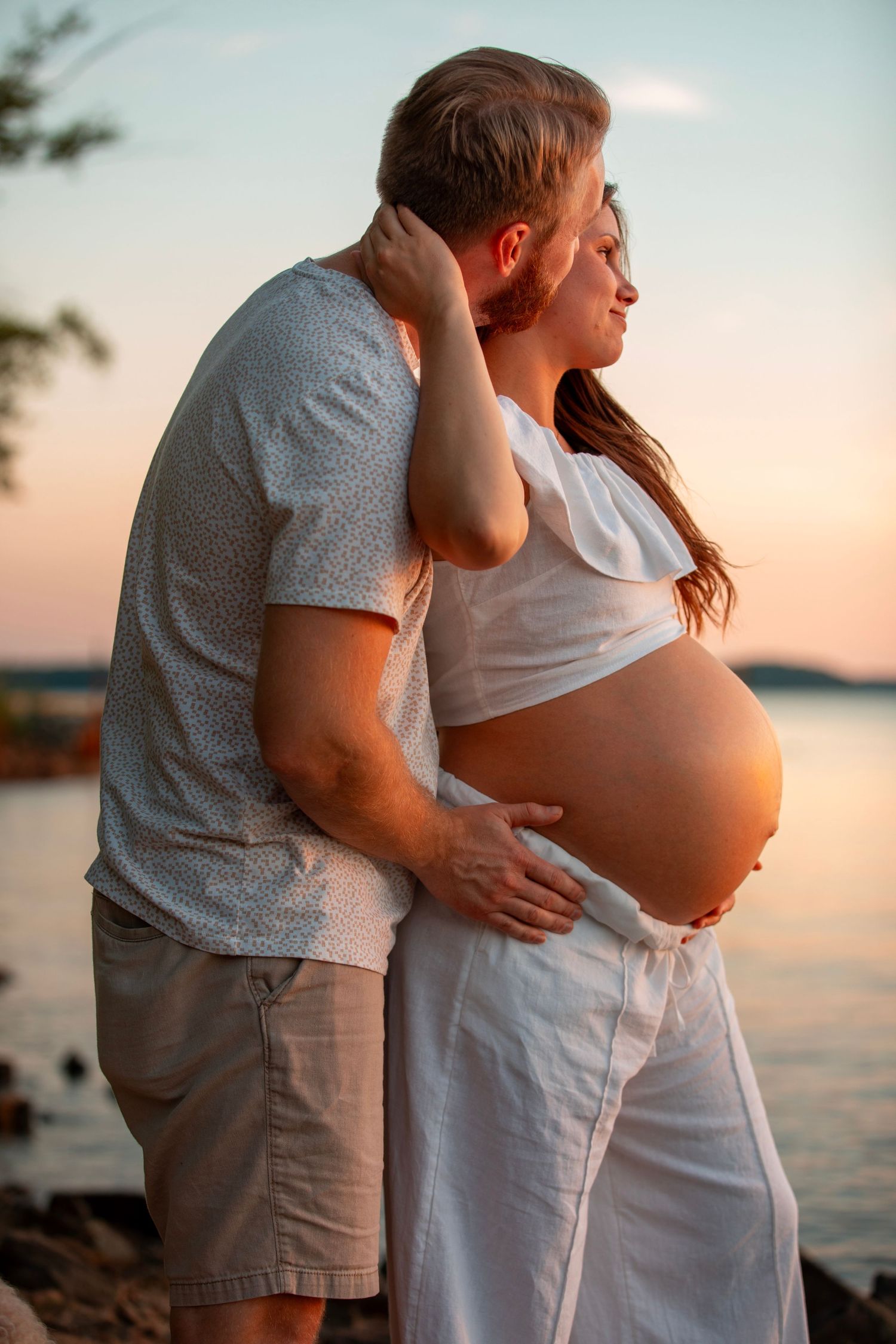 Couple embraces during sunset at the beach while expecting a baby, creating a romantic maternity silhouette.