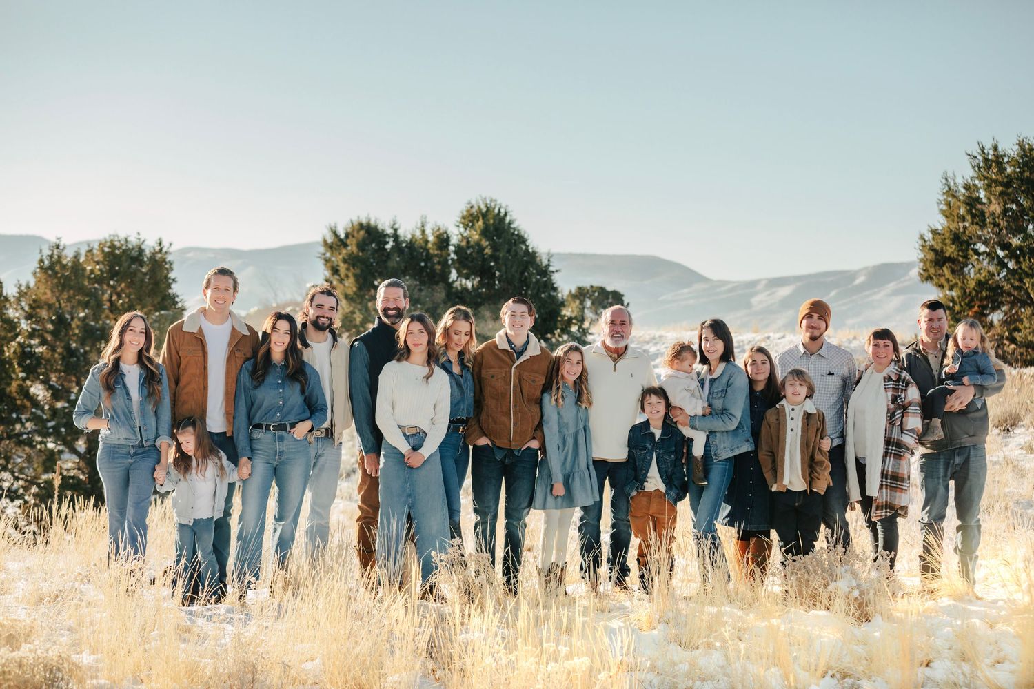 A panoramic group photo of people posing in casual denim outfits against a mountain landscape.