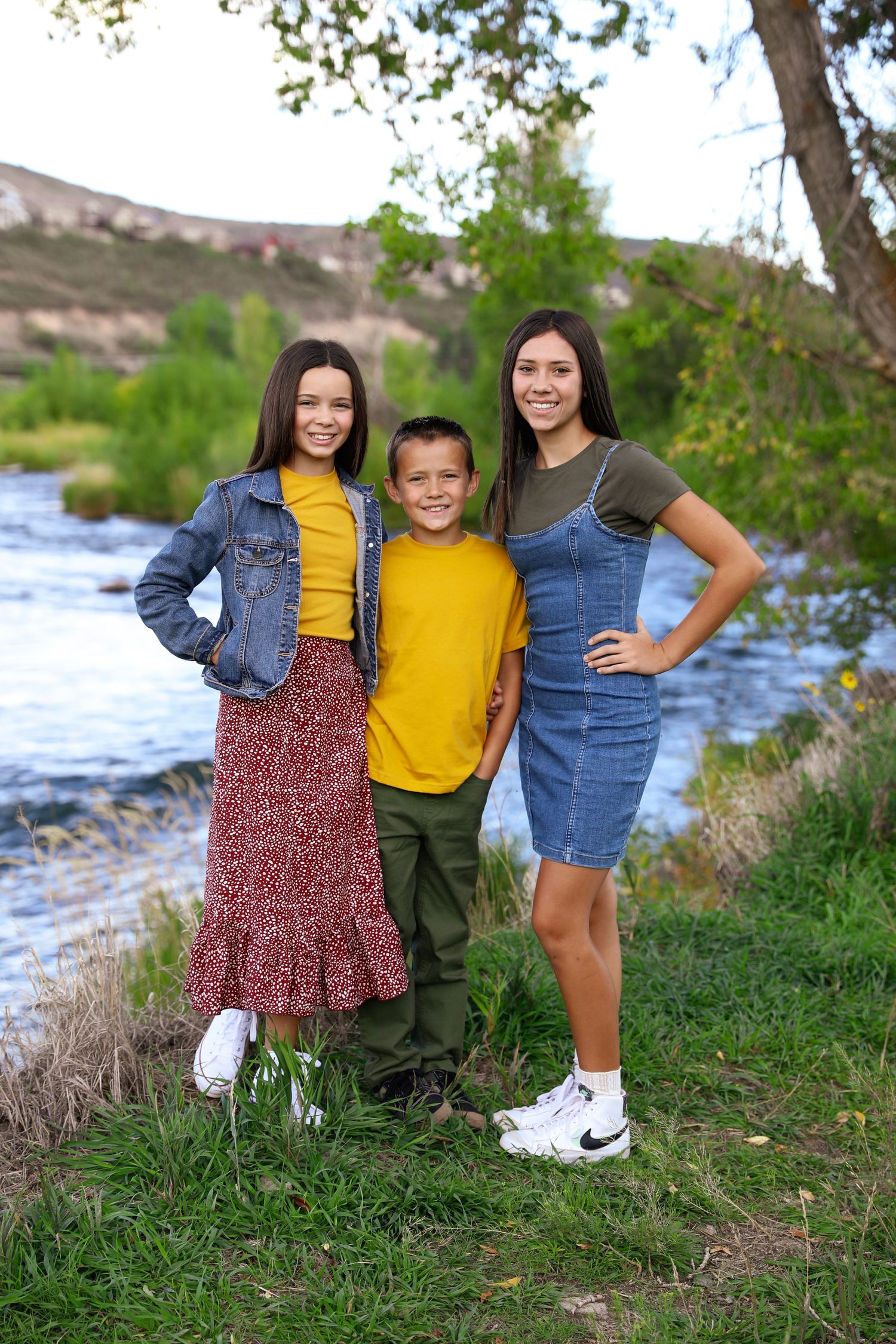 Children posing together by a riverside on a sunny day wearing casual summer outfits.