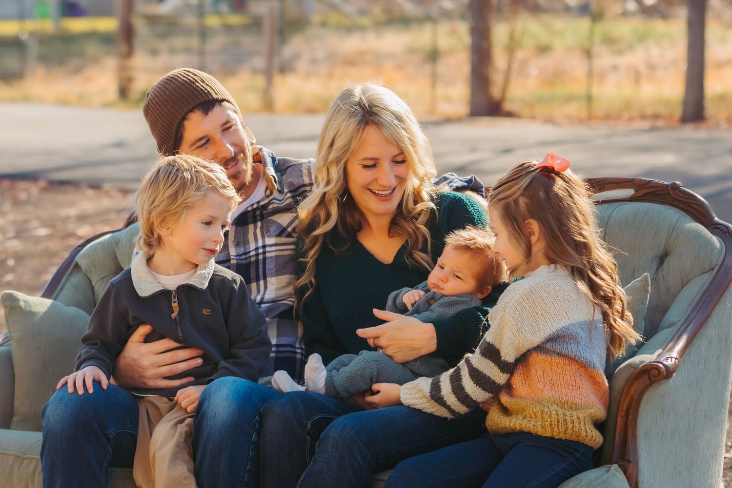 Family of five cuddles together on outdoor couch during autumn afternoon.