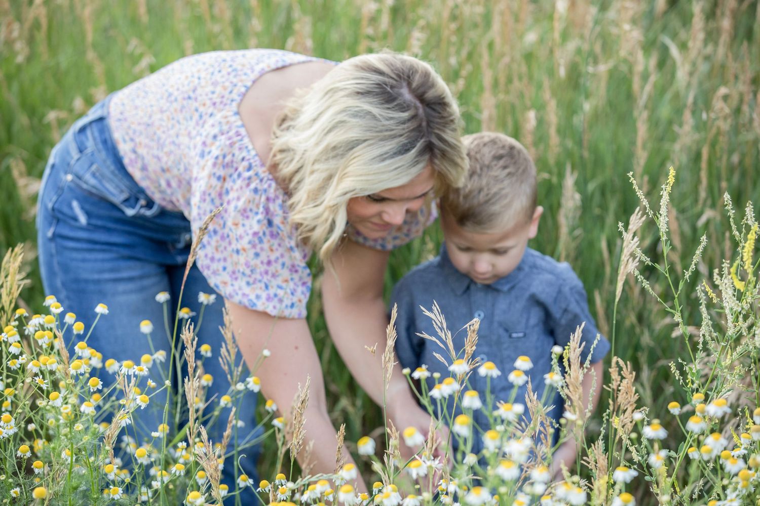 Mother and son pick wildflowers in a lush green meadow during springtime.