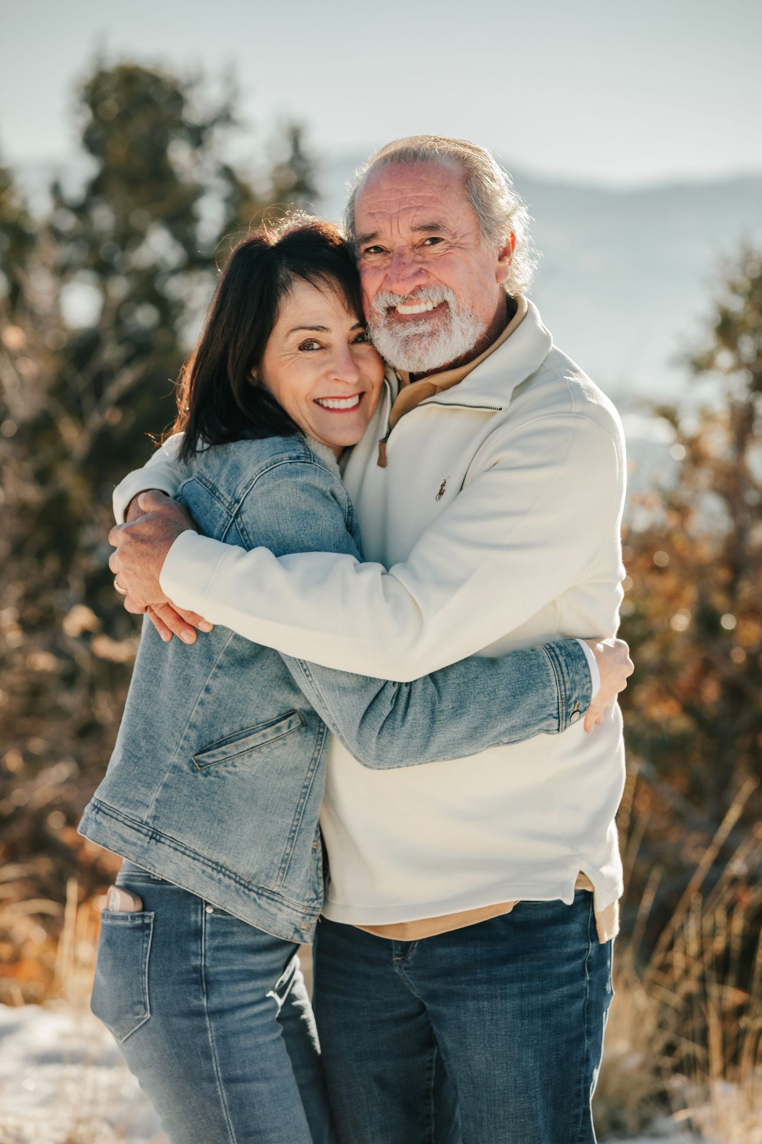 A couple embraces outdoors on a sunny day with mountains in the background.