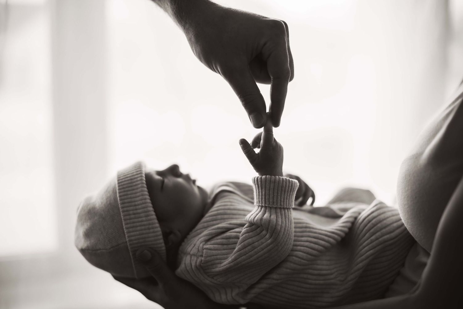 Black and white image of a tiny hand grasping an adult finger in an intimate newborn moment.