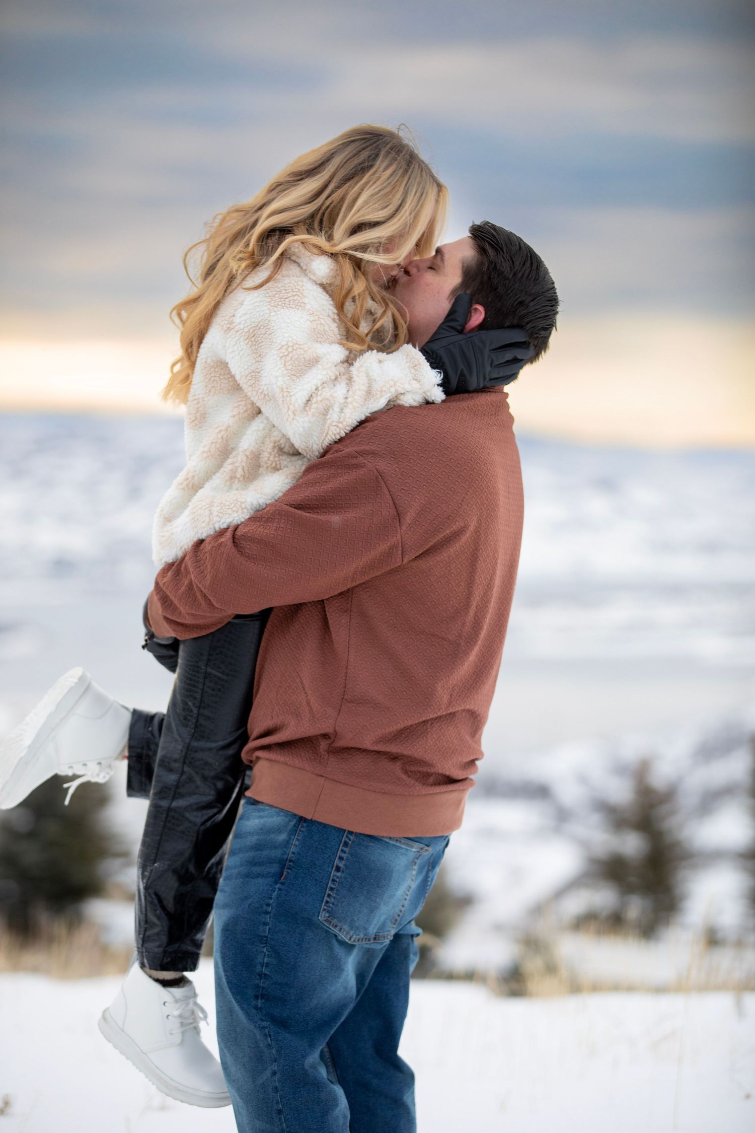 A romantic winter scene shows a couple embracing in snowy terrain at twilight.