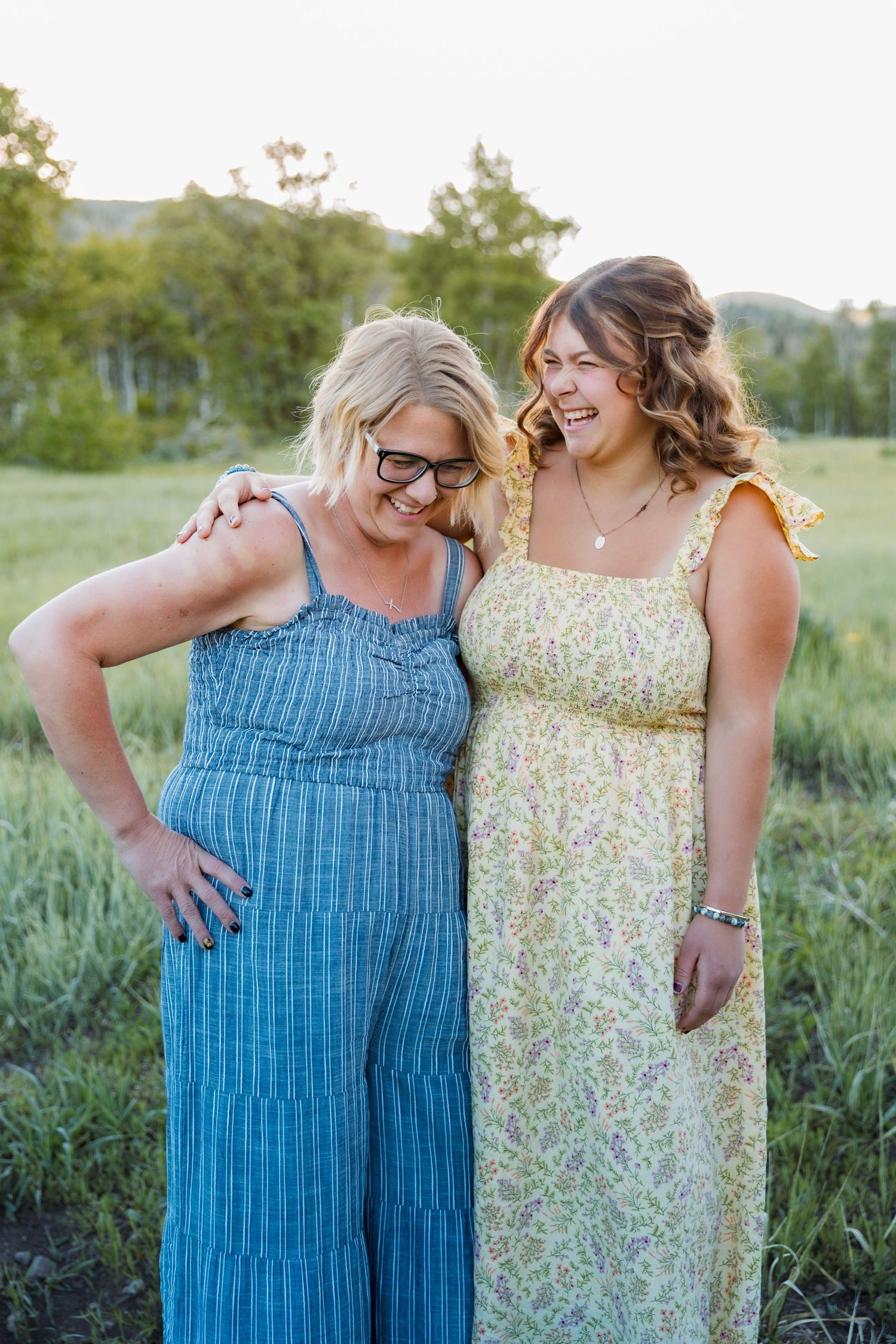 Mother & Daughter share a joyful laugh while standing together in a grassy field on a sunny summer day.