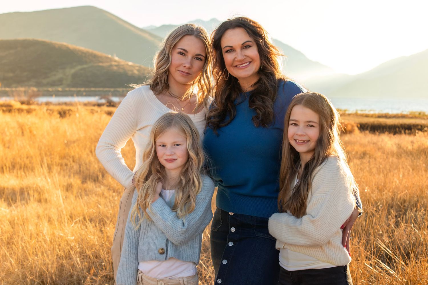 Family stands together in a golden field at sunset against mountain backdrop during a photo session.