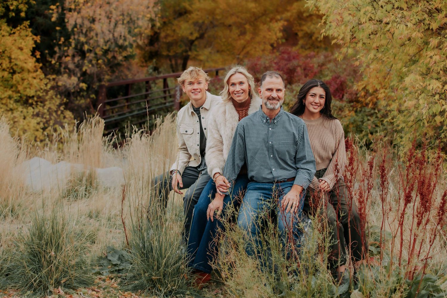 A group poses together outdoors during autumn with colorful fall foliage and tall grass in the background.