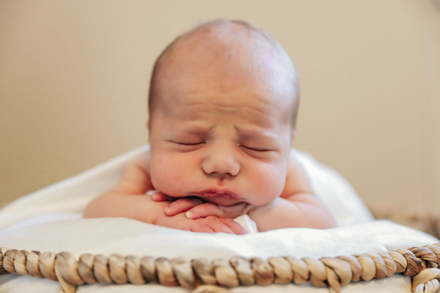A sleeping newborn baby resting peacefully on a soft beige blanket.