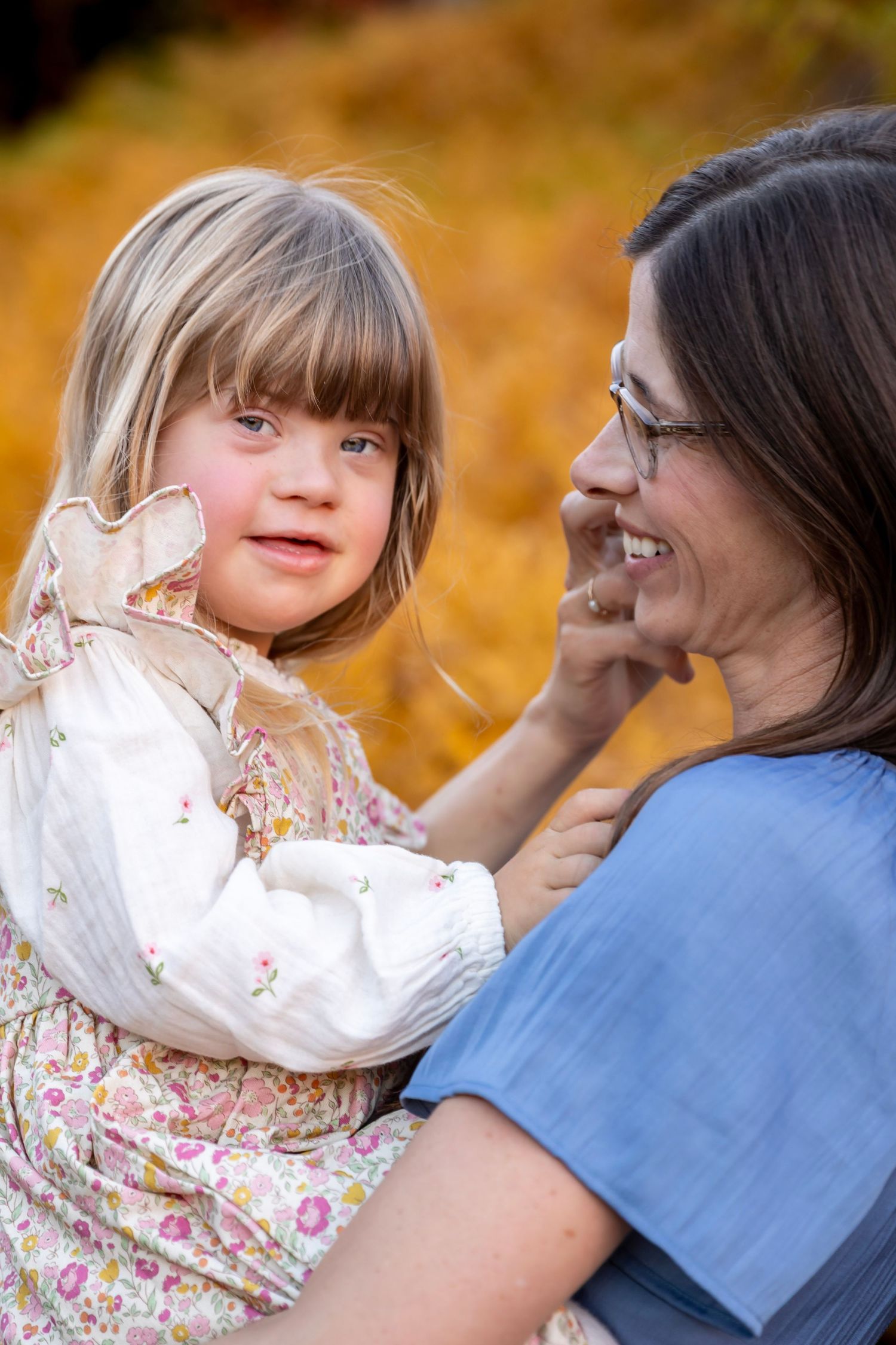 A young child wearing a floral dress smiles alongside a caregiver on a warm autumn day.