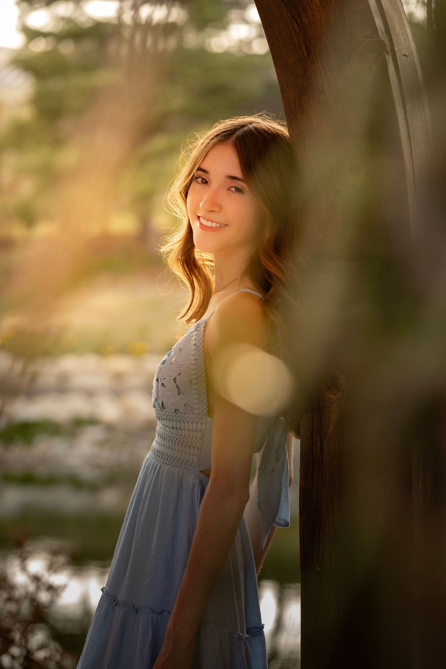A dreamy portrait of someone in a light blue dress standing outdoors at sunset with bokeh lighting effects.
