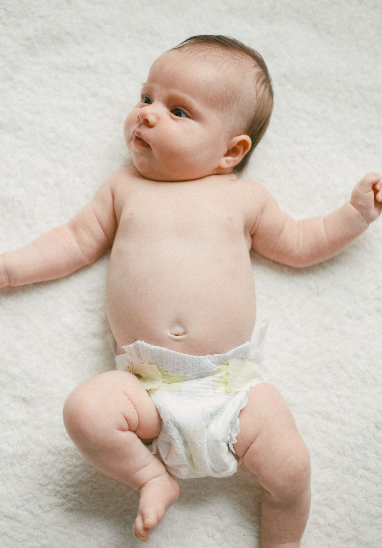 Infant wearing a diaper lying on white blanket with outstretched arms.
