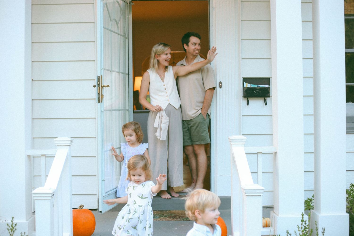 A family gathers on the front steps of their white house on a sunny day.