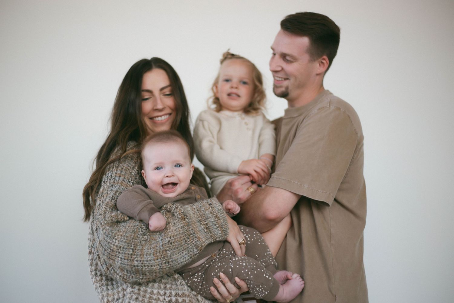Family cuddles together while wrapped in a cozy knit blanket during intimate photo session.